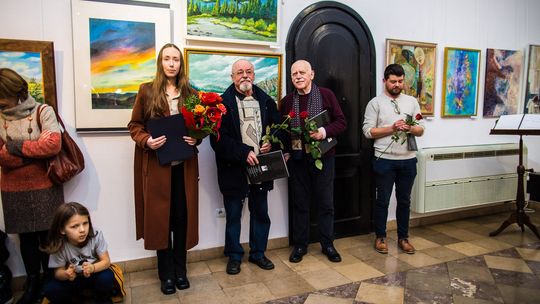 artyści stojący pod ścianą z różami podczas wystawy w Gorlicach