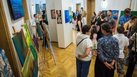 zdjęcie przedstawia grupę osób między obrazami powieszonymi w holu Gorlickiego Centrum Kultury