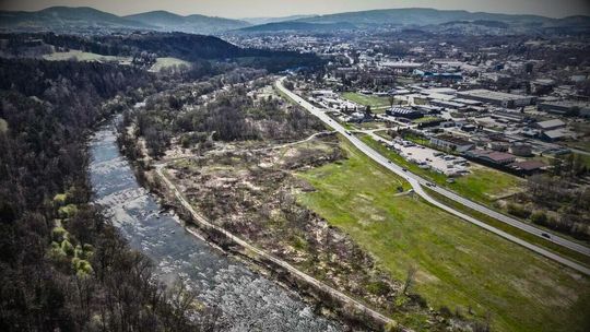 zdjęcie przedstawia rzekę, łąki i drogę, a za nią zabudowania miejskie