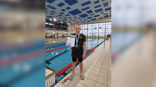 zdjęcie przedstawia chłopca z dyplomem i medalem na brzegu basenu
