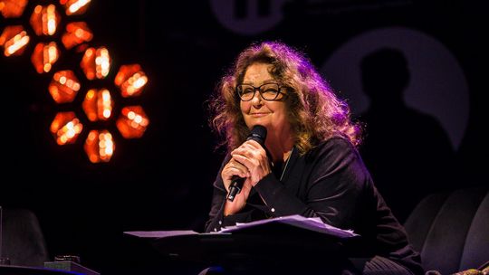 zdjęcie przedstawia kobietę z długimi włosami z mikrofonem przy ustach