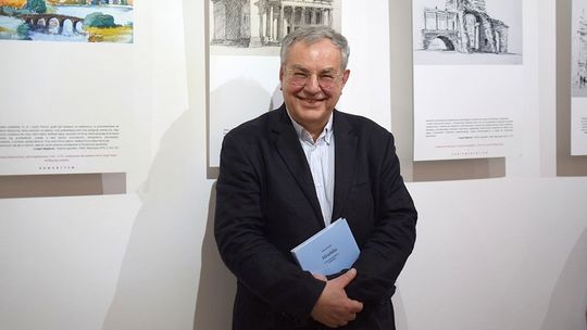 zdjęcie przedstawia uśmiechniętego mężczyznę w okularach, w tle grafiki, obrazy