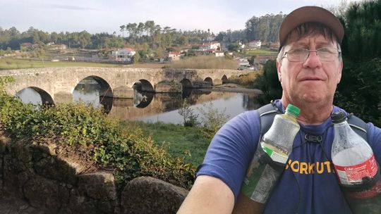 mężczyzna w czapeczce z plecakiem, w tle most