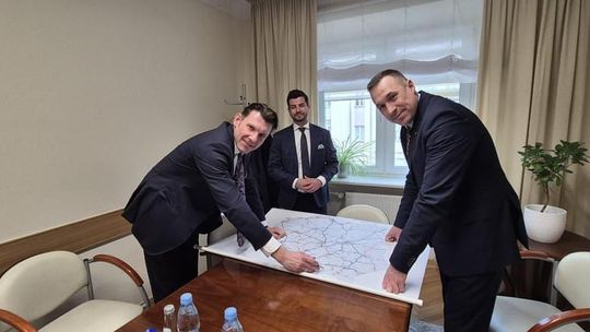 trzech mężczyzn w garniturach pochylonych nad mapą Polski