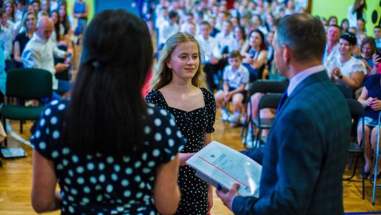 dziewczyna odbierająca świadectwo na koniec roku szkolnego z rąk dorosłych