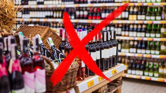 zdjęcie przedstawia wnętrze sklepu z butelkami alkoholu na półkach i czerwony krzyż na pierwszym planie