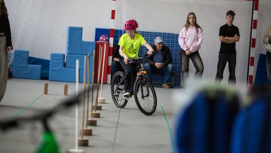 zdjęcie przedstawia dziewczynkę jadącą na rowerze między tyczkami