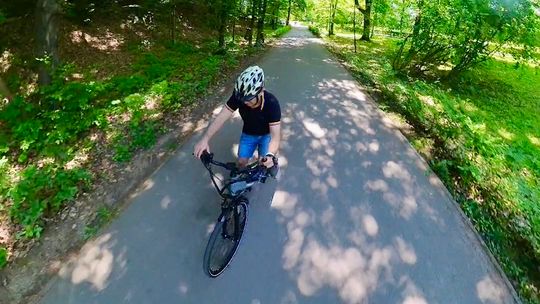 Mężczyzna jadący na rowerze w kasku. Jedzie przez park