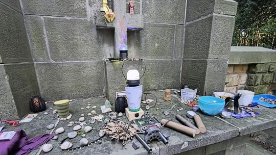 zdjęcie przedstawia różne drobne przedmioty postawione na nagrobku z krzyżem