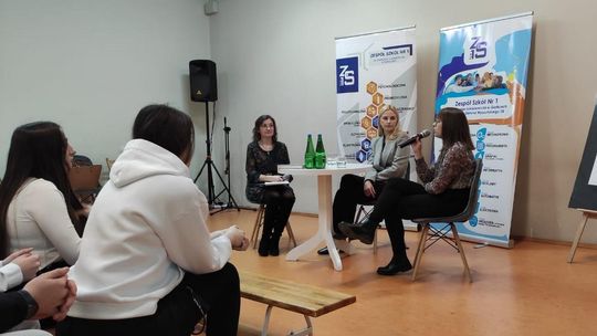 trzy kobiety siedzące na podwyższeniu podczas spotkania autorskiego w Zespole Szkół nr 1 w Gorlicach