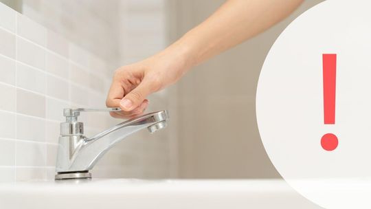 Zdjęcie przedstawia dłoń na kranie w łazience