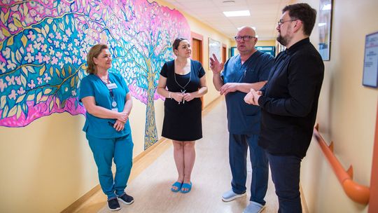 zdjęcie przedstawia cztery osoby stojące na korytarzu szpitala, na ścianie namalowane kolorowe drzewo