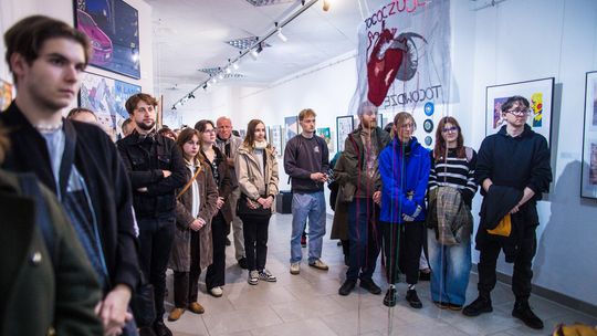 grupa osób stojąca w pomieszczeniu, w tle obrazy i fotografie na ścianach