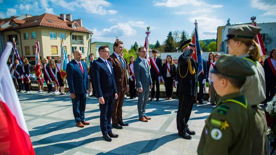 zdjęcie przedstawia mężczyzn w garniturach stojących w otoczeniu pocztów sztandarowych