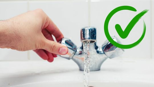 dłoń męska odkręcająca kurek z wodą nad umywalką, z kranu leci woda, obok zielony check box