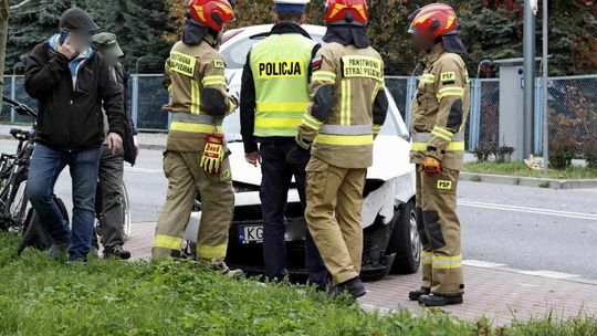 zdjęcie przedstawia uszkodzony pojazd a przed nim strażacy i policjanci