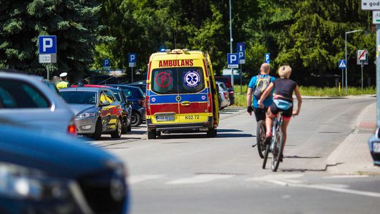 zdjęcie przedstawia karetkę pogotowia stojącą na jezdni obok policjant i rowerzyści