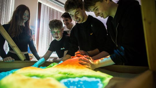 zdjęcie przedstawia chłopców usypujących górkę z piasku