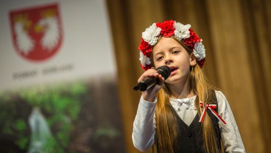 zdjęcie przedstawia śpiewającą dziewczynkę, na głowie ma biało-czerwony wianek