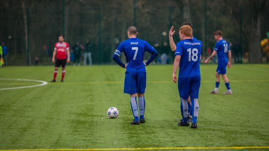trzech piłkarzy w niebieskich koszulkach stoi przed piłką