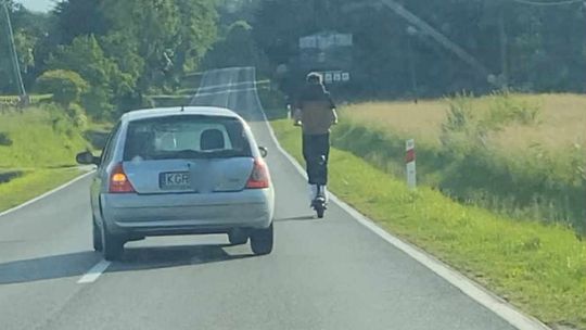 zdjęcie przedstawia samochód wyprzedzający osobę jadącą po ulicy na hulajnodze