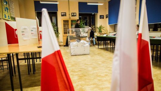 urna wyborcza w lokalu, na pierwszym planie flaga polski