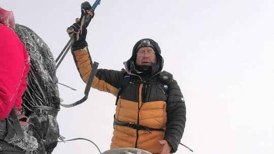 zdjęcie przedstawia mężczyznę w kurtce zimowej i czekanem na górze w śniegu