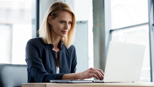 Jak zyskać więcej czasu dzięki automatyzacji rozliczeń? zdjęcie przedstawia kobietę siedzącą przy stole, patrzącą w laptop