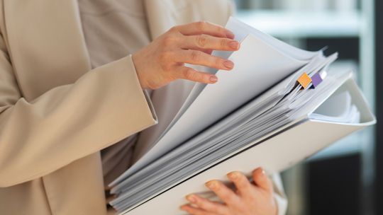 JPK CIT w prostych słowach – co musisz przygotować jako przedsiębiorca? zdjęcie przedstawia segregator z dokumentami trzymanymi przez kobietę w garniturze