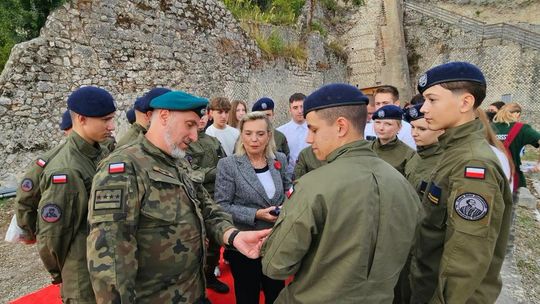 grupa osób w mundurach i z beretami wojskowymi, w tle mury i skały