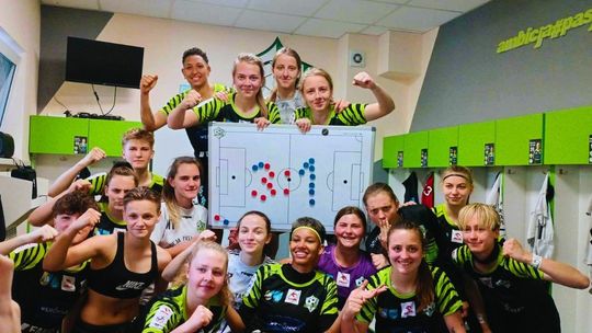 drużyna dziewcząt w szatni cieszy się ze zwycięstwa, trzymają tablicę na której jest napisane 3:1