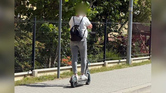 zdjęcie przedstawia osobę jadącą chodnikiem na hulajnodze