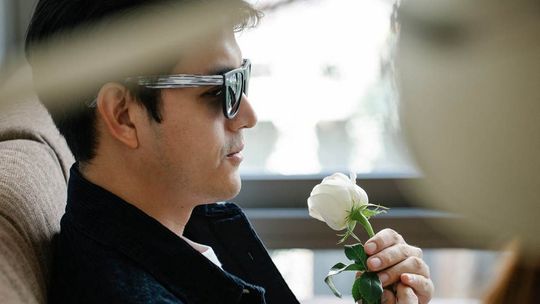 Klasyka i nowoczesność w męskich kompozycjach zapachowych. Polecane produkty zdjęcie przedstawia mężczyznę w okularach z białym kwiatkiem w ręce