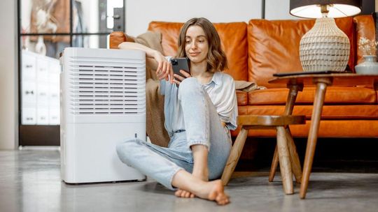 kobieta siedząca na podłodze obok przenośnego klimatyzatora