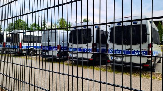 zdjęcie przedstawia kilka radiowozów policji ustawionych w rzędzie, widok przez kratki ogrodzenia