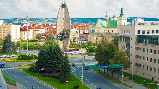 Widok centrum Rzeszowa. Na pierwszym planie znajduje się rondo z Pomnikiem Czynu Rewolucyjnego otoczonym zielenią i ulicami.
