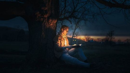 mężczyzna siedzący pod drzewem w nocy czytający książkę