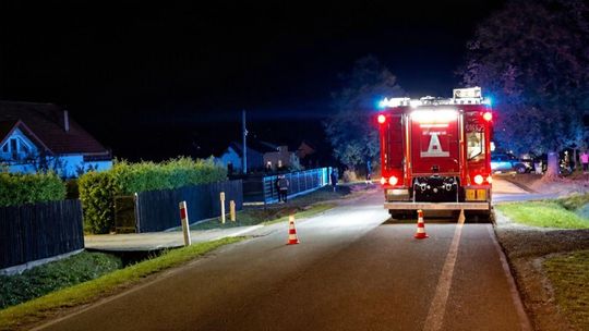 samochód straży pożarnej stojący na jezdni, obok ogrodzenia domów, zdjęcie w nocy