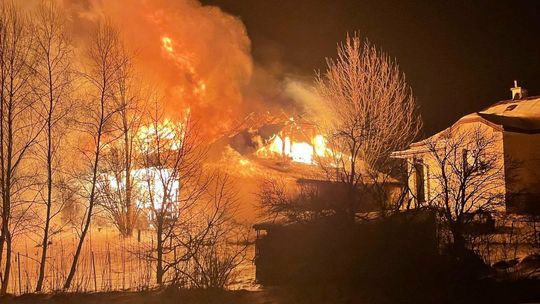 zdjęcie przedstawia płonący budynek za drzewami