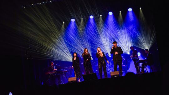 zdjęcie przedstawia kilka osób na scenie w blasku świateł podczas koncertu