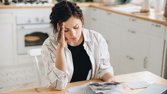 Mała pożyczka na remont mieszkania — ile i gdzie można pożyczyć? zdjęcie przedstawia kobietę siedzącą przy stole trzymającą w ręku rachunki