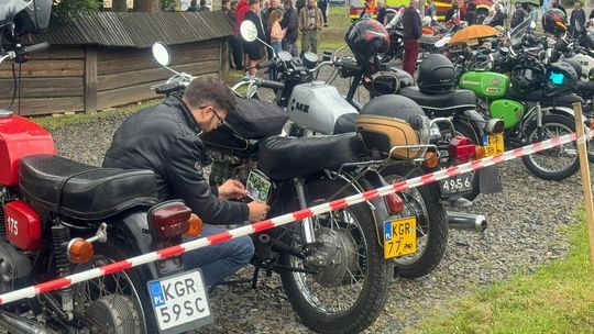 zdjęcie przedstawia motocykle ustawione w rzędzie, mężczyzna nakleja naklejkę na jednym z nich