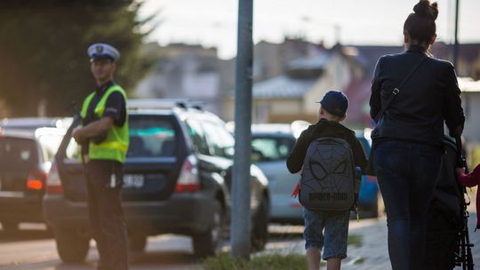 zdjęcie przedstawia dziecko i kobietę pchającą wózek, widok od tył, w tle policjant na ulicy w Gorlicach