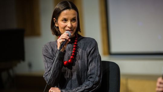 zdjęcie przedstawia kobietę z czerwonymi koralami i mikrofonem przy ustach