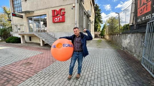 Mężczyzna stojący z pomarańczową piłką przed budynkiem DG Art