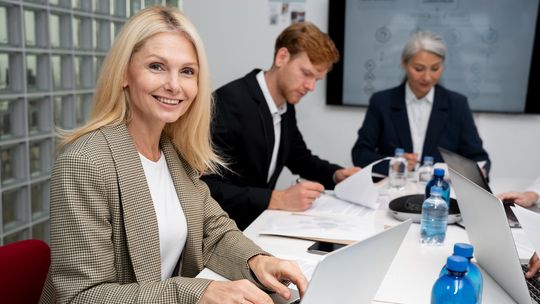 kobieta siedząca przed komputerem uśmiechająca się do aparatu
