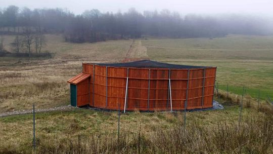 zdjęcie przedstawia drewnianą konstrukcję na łące