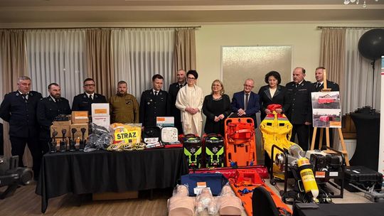 zdjęcie przedstawia grupę ludzi przy stole na którym leżą pakunki i urządzenia