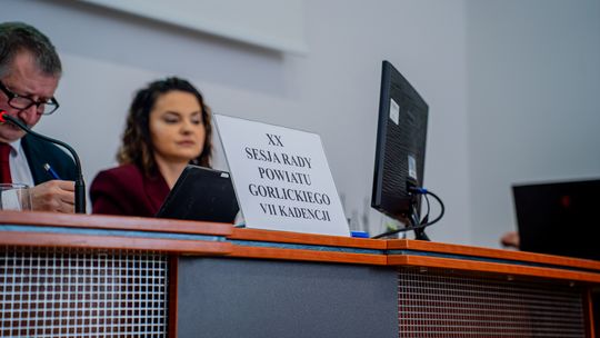 Opieka zdrowotna w powiecie gorlickim. POZ, poradnie i ratownictwo tematem sesji w starostwie zdjęcie przedstawia dwie osoby przy stole, przed nimi tabliczka z napisem XX sesja rady powiatu gorlickiego