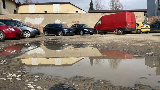 zdjęcie przedstawia kałużę na parkingu, w tle stoją samochody